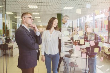 Dört iş adamı tartışıyor ve plan yapıyor. Cam duvar işareti ve çıkartmaların önünde. Başlangıç ofisi