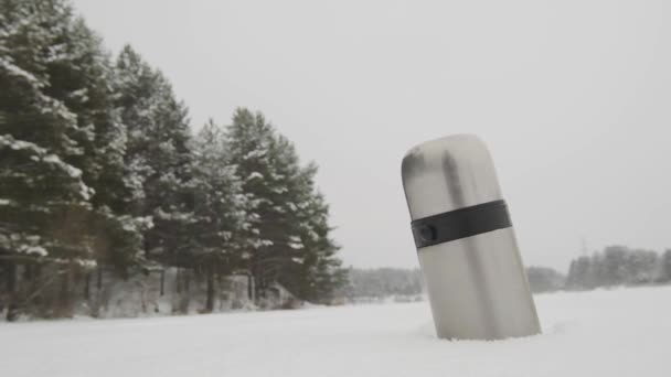 Thermoskanne im Schnee vor dem Hintergrund fallenden Schnees — Stockvideo