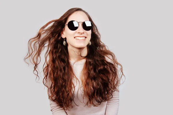 Mujer joven morena sonriente con gafas de sol retro posando y mirando a la cámara sobre fondo blanco. Feliz chica alegre . — Foto de Stock