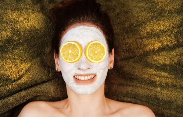 젊은 미소 여자 얼굴 마스크와 눈에 레몬의 조각. 여성 피부 관리. — 스톡 사진