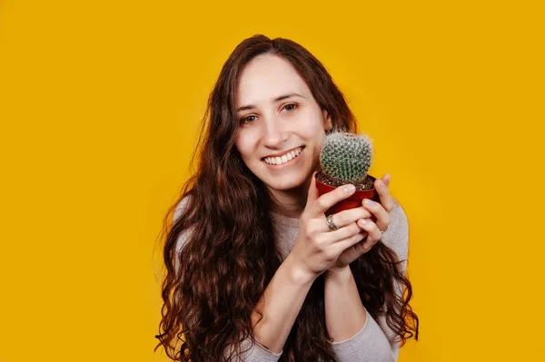 Joven alegre sonriente con el pelo largo rizado sosteniendo un cactus en las manos . — Foto de Stock