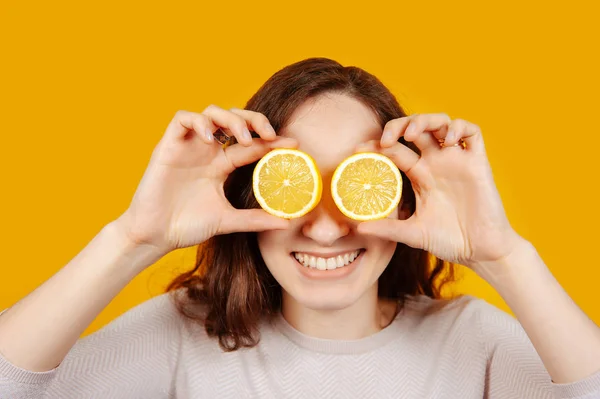 Wanita muda cantik dengan lemon setengah dekat mata pada latar belakang kuning — Stok Foto