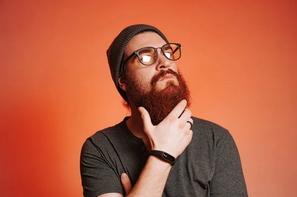 Homem barbudo com óculos tocando sua barba e olhando para o lado, tiro estúdio — Fotografia de Stock