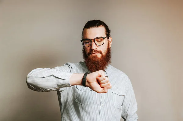 Barbuto hipster uomo in casual indossare occhiali e guardando il suo smartwatch . — Foto Stock