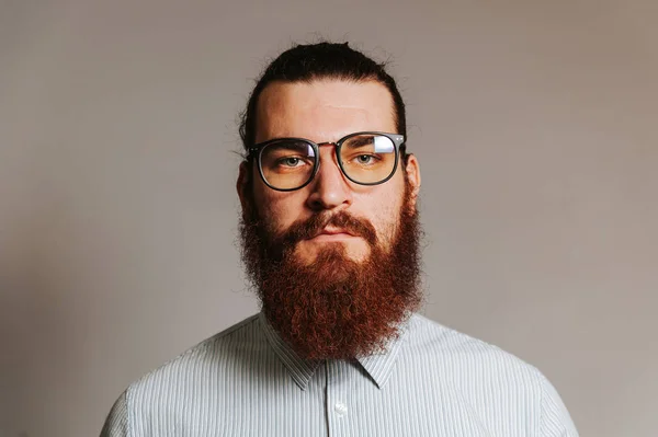 Primer plano retrato de joven barbudo hipster hombre en casual con gafas de ojo mirando con confianza en la cámara sobre fondo gris — Foto de Stock