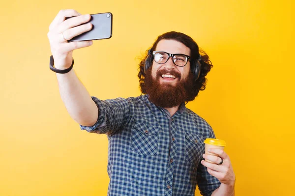 Hombre barbudo alegre tomando una selfie y sosteniendo una taza de café o —  Fotos de Stock