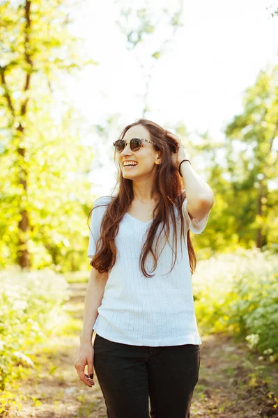 Uśmiechający się młoda kobieta, noszenie okularów przeciwsłonecznych i dotykając jej włosy w — Zdjęcie stockowe