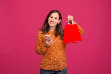 Image of young happy woman holding smartphone and shopping bags, online shopping