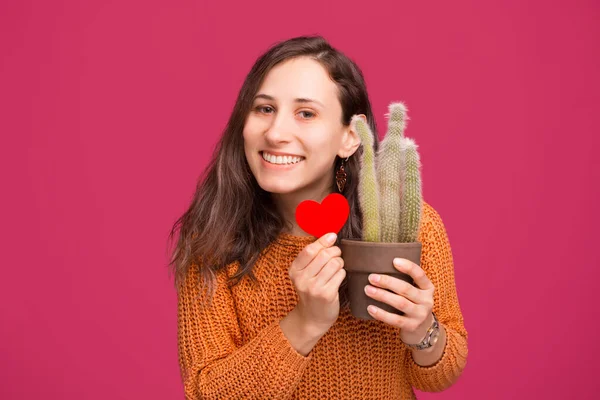Photo of happy woman holding cactus plant and red heart shape — Zdjęcie stockowe