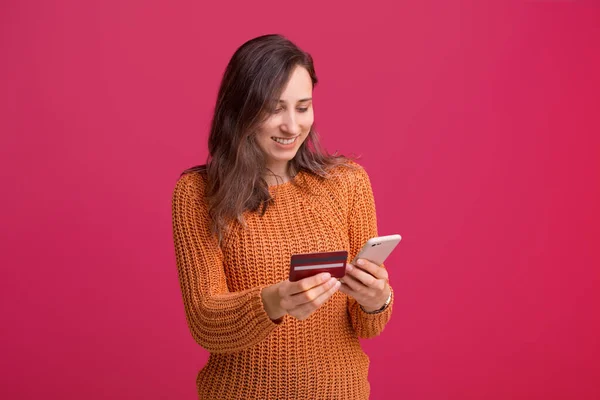 Happy woman in yellow sweater buying something with credit card and smartphone, web banking — Stock fotografie