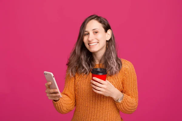 Jovem mulher encantadora segurando smartphone e xícara de café para ir — Fotografia de Stock