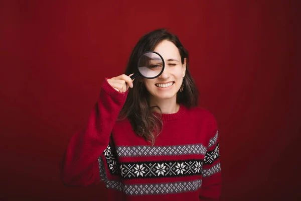 Jonge vrouw kijken u door een vergrootglas staande over rode achtergrond — Stockfoto