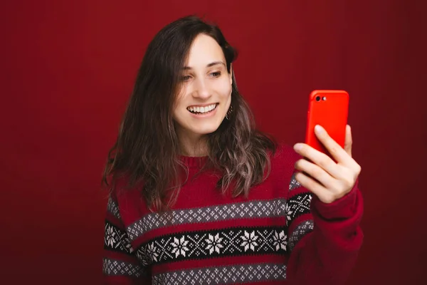 Jovem mulher encantadora em camisola de inverno em pé sobre fundo vermelho e tomando selfie — Fotografia de Stock