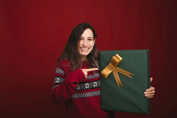 Glückliche junge Frau im roten Pullover zeigt auf große grüne Geschenkschachtel für Weihnachten — Stockfoto
