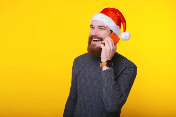 산타 클로스 모자를 쓰고 스마트폰으로 얘기하는 밝은 미소를 가진 잘생긴 남자 — 스톡 사진