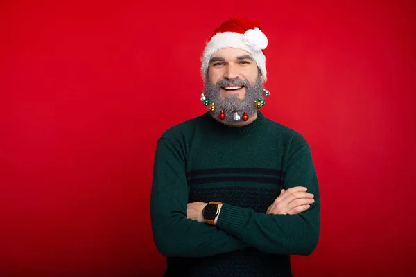 Süslü beyaz sakallı, Noel Baba şapkası takmış kollarını kavuşturup kameraya kendinden emin bir şekilde bakan neşeli bir adamın portresi. — Stok fotoğraf