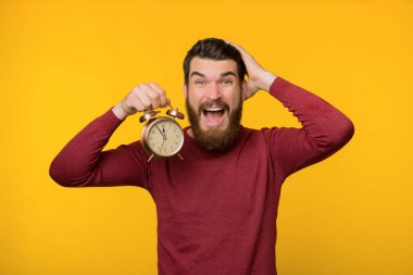 Sinirli sakallı bir adamın saat tutarken çekilmiş bir fotoğrafı. 