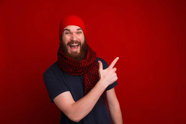 Szczęśliwy facet w czerwonym kapeluszu i szaliku, wskazując podczas patrzenia — Zdjęcie stockowe