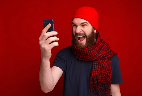 Photo of screaming bearded guy, wearing red hat and scarf, using — Stockfoto