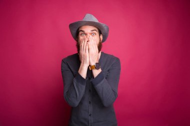 Sakallı genç adam pembe arka plandaki kameraya hayret içinde bakıyor..