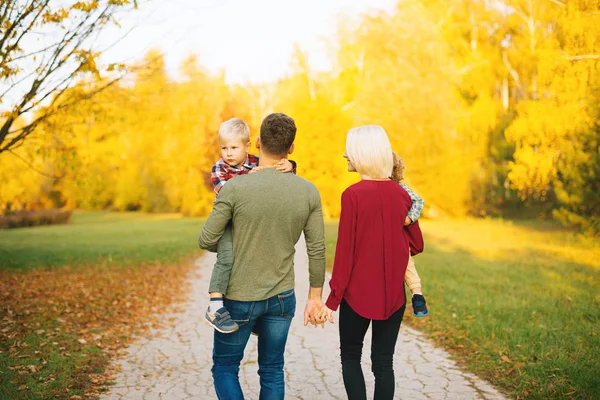 Young happy family are walking through fall  park. Parents are holding their children. — Stock Photo, Image