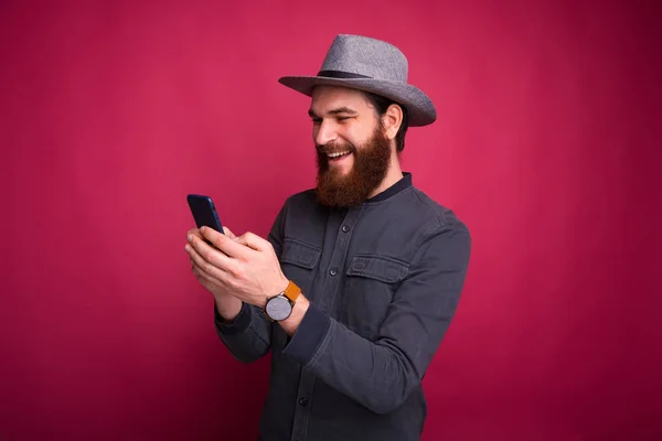Glada unga man ler och tittar i sin telefon nära rosa vägg. — Stockfoto