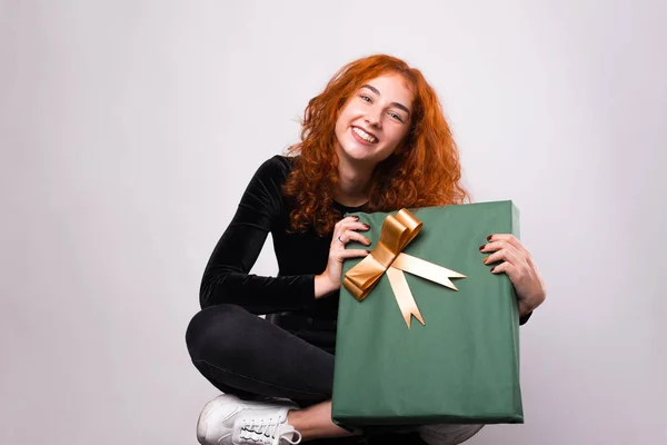 Lächelnde junge Frau hält ein grünes Geschenk in der Nähe der weißen Wand. — Stockfoto