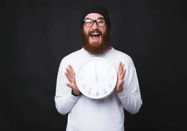 Φωτογραφία από έκπληκτος νεαρός άνδρας με γενειάδα κρατώντας μεγάλο λευκό ρολόι — Φωτογραφία Αρχείου