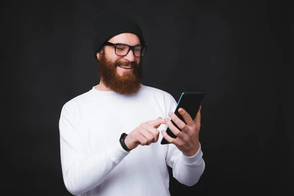 Retrato del hombre barbudo de moda feliz usando su tableta sobre fondo oscuro — Foto de Stock