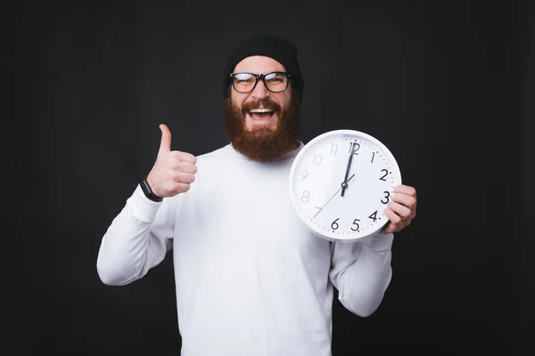 Foto de un joven alegre mostrando los pulgares hacia arriba y sosteniendo un gran reloj blanco — Foto de Stock