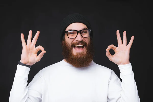 Foto de un hombre barbudo alegre mostrando un gesto aceptable sobre fondo oscuro — Foto de Stock