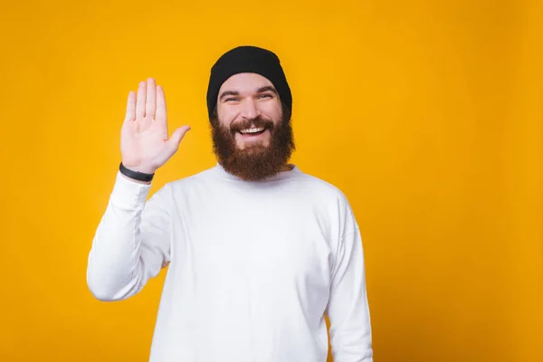 Foto van trendy jonge hipster man maken Hallo gebaar staande over gele achtergrond — Stockfoto