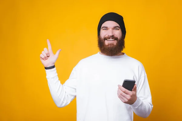 Retrato de un joven sosteniendo un teléfono inteligente y apuntando hacia el espacio de copia — Foto de Stock