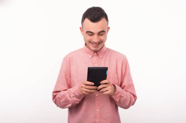 Mutlu genç adam beyaz duvarın üzerinde tablet kullanıyor.