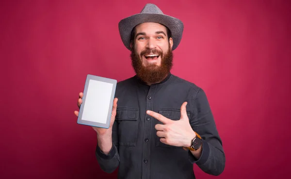 Sorprendido joven barbudo apuntando a la pantalla en blanco en la tableta — Foto de Stock