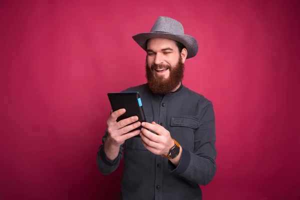 Glad man med skägg bär grå hatt och använder sin tablett — Stockfoto