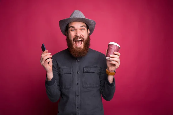 Hombre feliz sosteniendo teléfono inteligente y taza de café para llevar — Foto de Stock