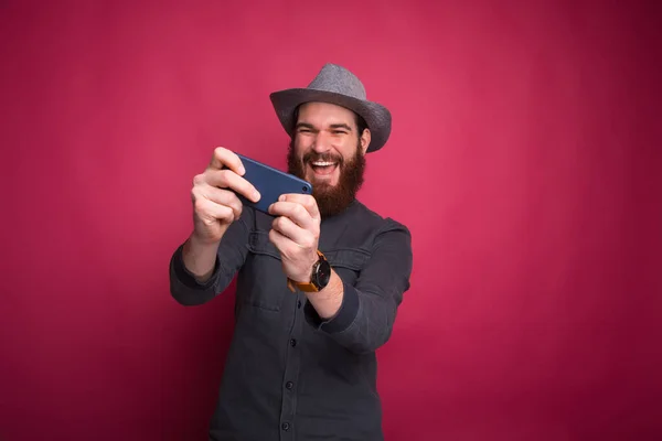 快乐的年轻大胡子男人在用智能手机玩游戏 — 图库照片