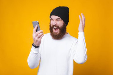 Sakallı kızgın adam akıllı telefondan bağırıyor, telefonda biriyle konuşuyor.