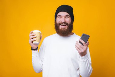 Kahvesinin tadını çıkaran ve elinde akıllı telefon tutan mutlu yakışıklı adam.