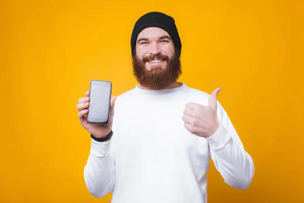 Portrait of trendy bearded hipster man holding smartphone and showing thumbs up — Stock Photo, Image