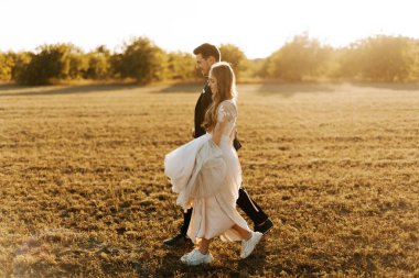 Neşeli genç çift gün batımında sahada yürüyor..