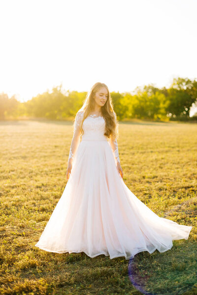 Young woman is dressed in a bridal dress and looking away in the field.