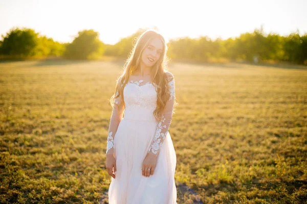 Mujer joven está en su vestido de novia y sonriendo en el campo . — Foto de Stock