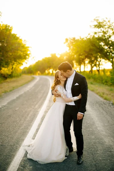 Joyful young couple is hugging on the road at sunset. — Stock Photo, Image
