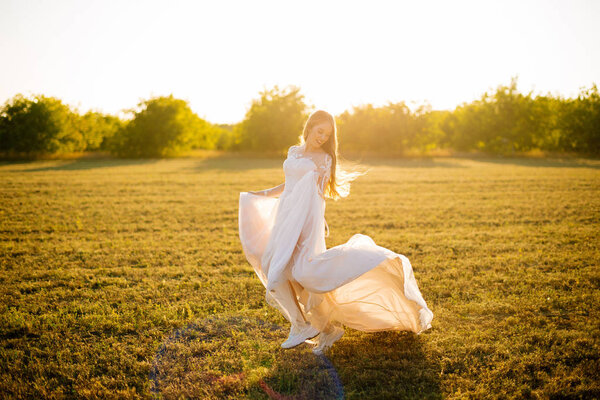 A bride is dancing and smiling in her bridal dress in the field.