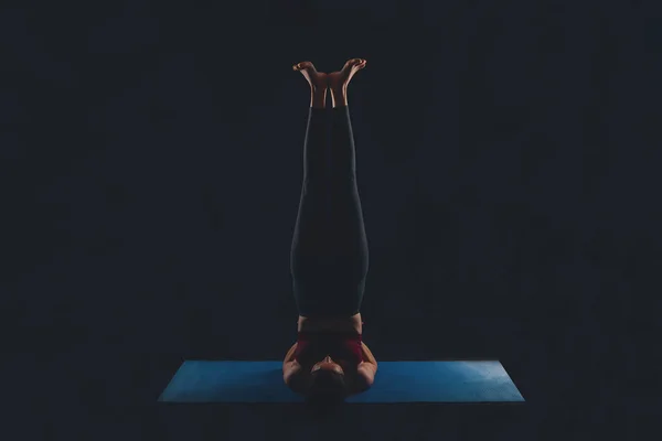 Jeune femme faisant du yoga en studio sur fond sombre, épaule, salamba sarvangasana — Photo