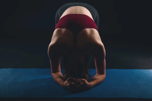 Jonge vrouw doet yoga in zwart studio, sirsasana headstand voorbereiding — Stockfoto