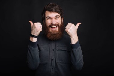 Şaşırmış sakallı adam gülümsüyor ve baş parmağını kaldırıyor.