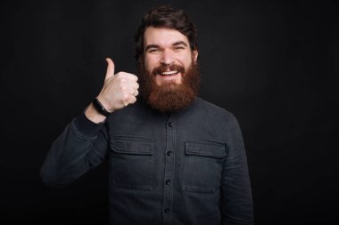 Gülümseyen mutlu adam karanlık arka planda başparmak gösteriyor.